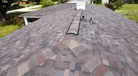 Newly installed multi-toned asphalt shingle roof on a residential home with clear sky and trees in background.
