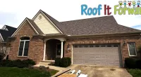 Brick single-story house with new roofing and attached garage under blue sky with Roof It Forward logo.