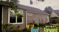 Side view of a suburban house with gray siding, a garden, and green grass under cloudy skies.