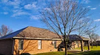 Single-story brick house with leafless trees on a sunny day under a blue sky with scattered clouds.