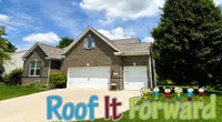 Modern brick house with gray roof under blue sky and Roof It Forward logo with cartoon kids on lawn