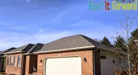 Modern brick house with white garage door under a bright blue sky and Roof It Forward logo in corner
