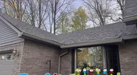Modern gray brick house with a clean dark shingle roof under leafless trees on a clear day