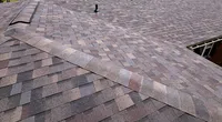 Newly installed dark gray asphalt shingle roof with a white cupola and surrounding green landscape on a sunny day