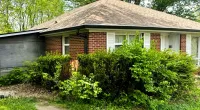 Brick house with a new roof surrounded by green bushes and trees on a sunny day