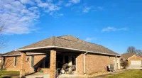 Single-story brick house with a covered patio and outdoor seating under a bright blue sky.