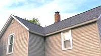 Two-story beige house with a dark shingle roof and clear blue sky in the background.