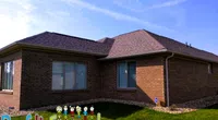 Modern brick house with freshly installed dark shingle roof under a clear blue sky with a grassy lawn.