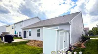 Suburban backyard with a white shed, green lawn, and cloudy sky with Roof It Forward cartoon text overlay.