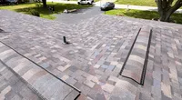 Newly installed asphalt shingle roof viewed from above with a suburban neighborhood and trees in the background.