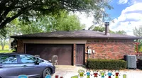 Brick house with brown garage door, parked car, tree, and Roof It Forward logo with cartoon children under blue sky.