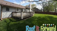 Sunny backyard with green grass and wooden deck attached to a single-story house under blue sky.