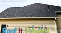 House with a dark shingled roof and colorful Roof It Forward sign featuring cartoon children on beige siding.