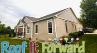 Residential house with beige siding and brick exterior with Roof It Forward logo featuring colorful children illustration.