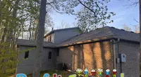 Residential house exterior in a wooded area with Roof It Forward colorful child logo at bottom