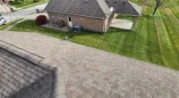 Aerial view of a residential neighborhood showing asphalt shingle roof, green lawns, and street with parked cars.