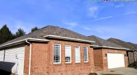 Single-story brick house with asphalt shingle roof under a clear blue sky, featuring white garage and windows.