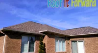 Brick house with new asphalt shingle roof under clear blue sky and Roof It Forward logo with children illustration.