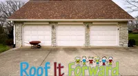 Three-car garage with white doors, stone pillars, and a brown roof with a wheelbarrow on the driveway.
