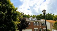 Suburban house with a brick facade, green lawn, mailbox, and the Roof It Forward logo with cartoon kids above.