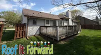 A suburban house with a wooden deck, fenced backyard, and green lawn under a partly cloudy sky.