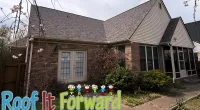 Brick house with gray shingle roof, double French doors, and greenery in front yard on a cloudy day