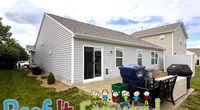 Backyard view of a gray house with patio, recycling bins, black outdoor bench, and Roof It Forward text overlay.