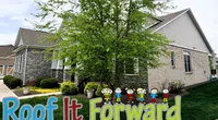 Suburban house with stone and brick exterior surrounded by greenery and Roof It Forward logo overlay with cartoon children.