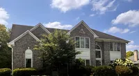 Large two-story brick house with white-framed windows, lush green lawn, and clear blue sky with clouds.