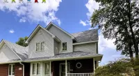 Two-story suburban house with gray roof, white siding, brick walls, and a front porch under a blue sky.