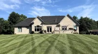 Large brick house with a neatly mowed lawn under a blue sky with light clouds.