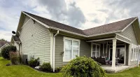 Modern single-story house with gray siding, brown roof, green lawn, and cloudy sky backdrop under daylight.