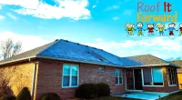Brick house with a newly installed blue shingle roof under a blue sky with clouds and Roof It Forward logo.