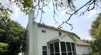 Two-story white house with a screened porch, green lawn, trees, and blue sky with scattered clouds.