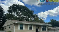 Suburban house with beige siding under a blue sky and clouds, Roof It Forward charity logo and message in corner.