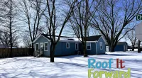 Blue house with bare trees casting shadows on snow-covered yard under clear winter sky.