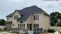Backyard view of a beige two-story house with a pool, deck, and overcast sky, promoting Roof It Forward charity.