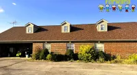 Brown shingle roof with dormer windows on a brick building under clear blue sky with Roof It Forward logo.