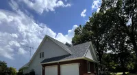 Two-car garage attached to a house with a sloped roof under a partly cloudy blue sky