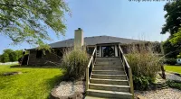 Brick house with new roof, wooden staircase, and landscaped yard under clear blue sky on a sunny day.