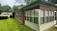 Brick single-story house with large windows, green lawn, and trees under a cloudy sky.