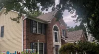 Two-story brick and siding house with large windows and trees framing the front yard under a cloudy sky