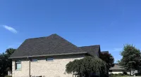 Brick house with new dark shingle roof under clear blue sky and green lawn on sunny day