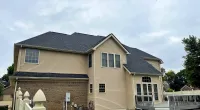 Two-story beige house with a dark gray roof and white fenced deck under a cloudy sky