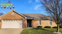 Brick house with a two-car garage under a clear blue sky and a large leafless tree on the lawn