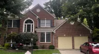 Two-story brick house with beige garage doors, arched front window, green lawn, and a red car parked in driveway.