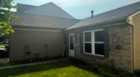 Backyard view of a suburban house showing brick and siding exterior, windows, door, and green lawn under clear sky