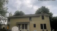 Backyard of a two-story yellow house with pool, patio furniture, and basketball hoop under cloudy sky.