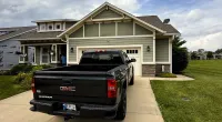 Black GMC Sierra truck parked in front of a modern suburban house with green siding and cloudy sky