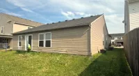Single-story beige house with fenced backyard and green lawn under a partly cloudy sky.